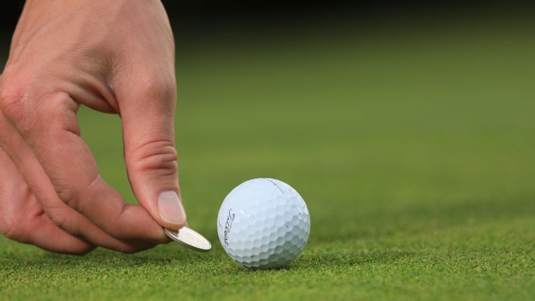Close up of a golfer placing a marker behind a golf ball on the putting green