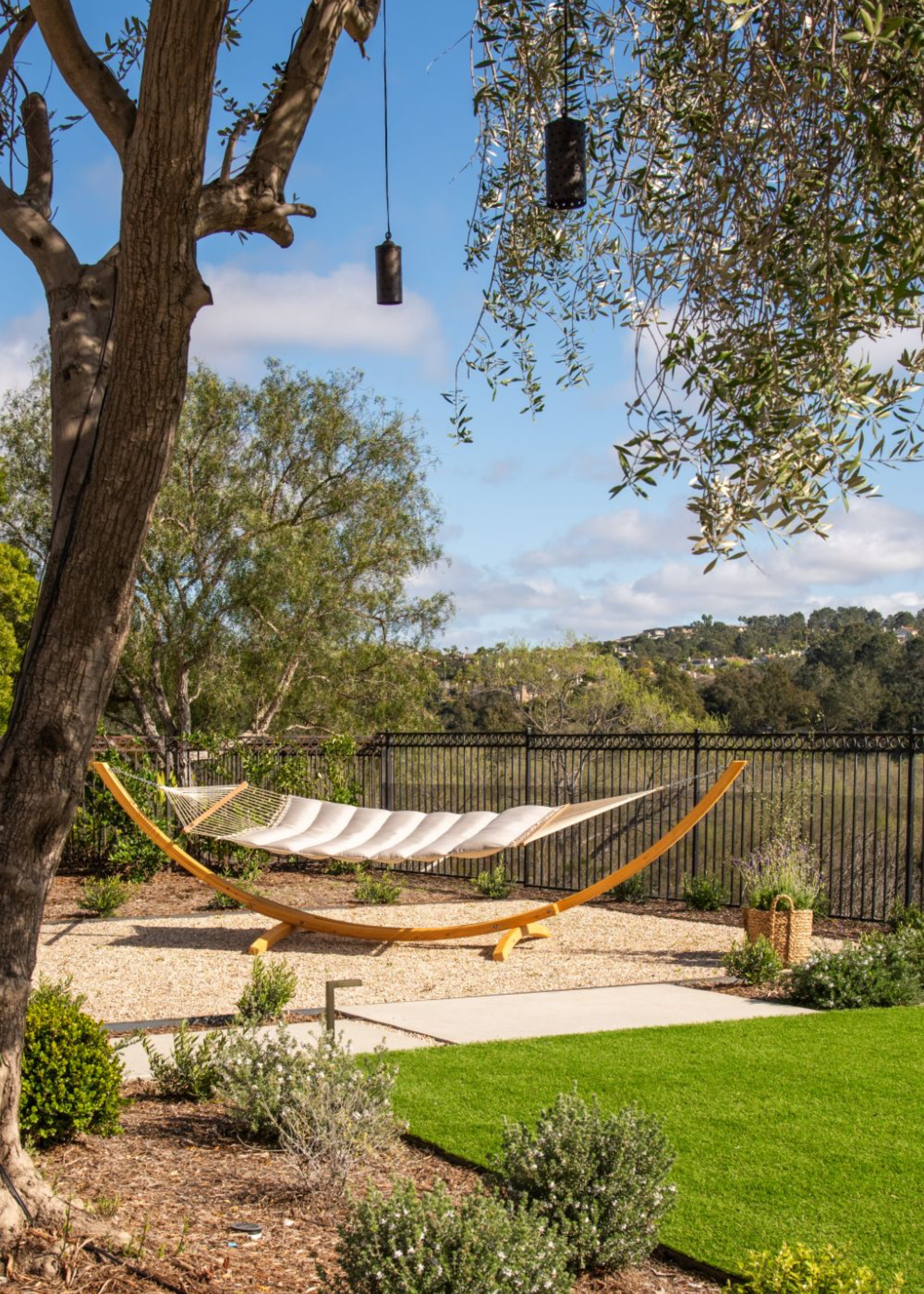 gravel area for hammock relaxing zone in the garden with a tree hanging above it. There are also plants scattered around as well as as turf laid out on the garden floor
