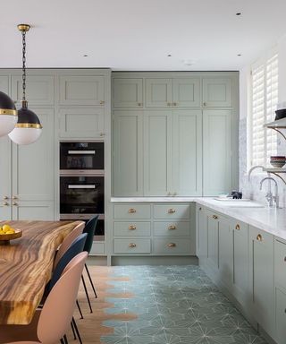 A mint green kitchen picture with hexagonal floor tiles and a wooden table.