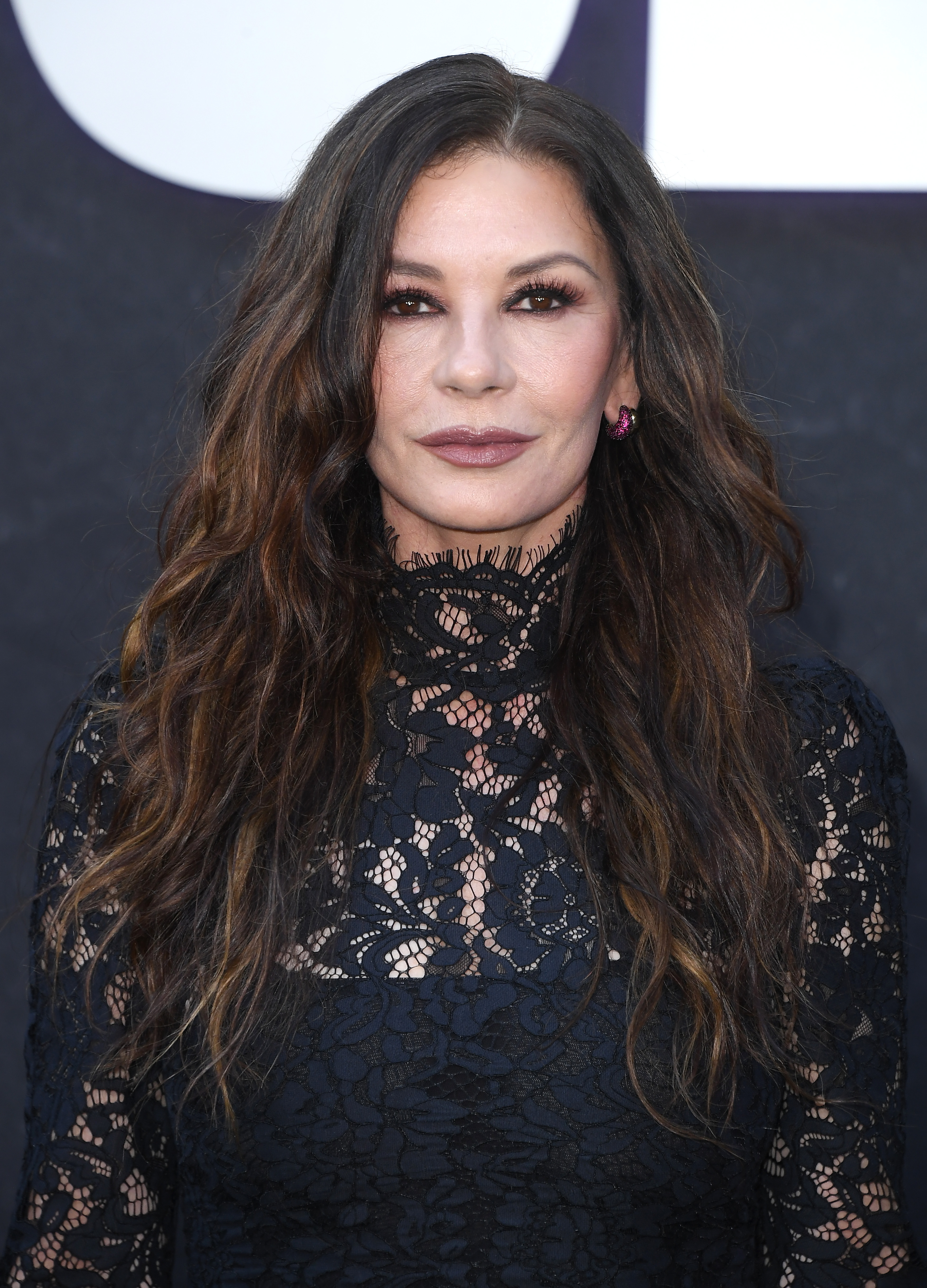 a photo of a white woman with long, brown hair posing on a red carpet wearing a black, lace dress in front of a black background