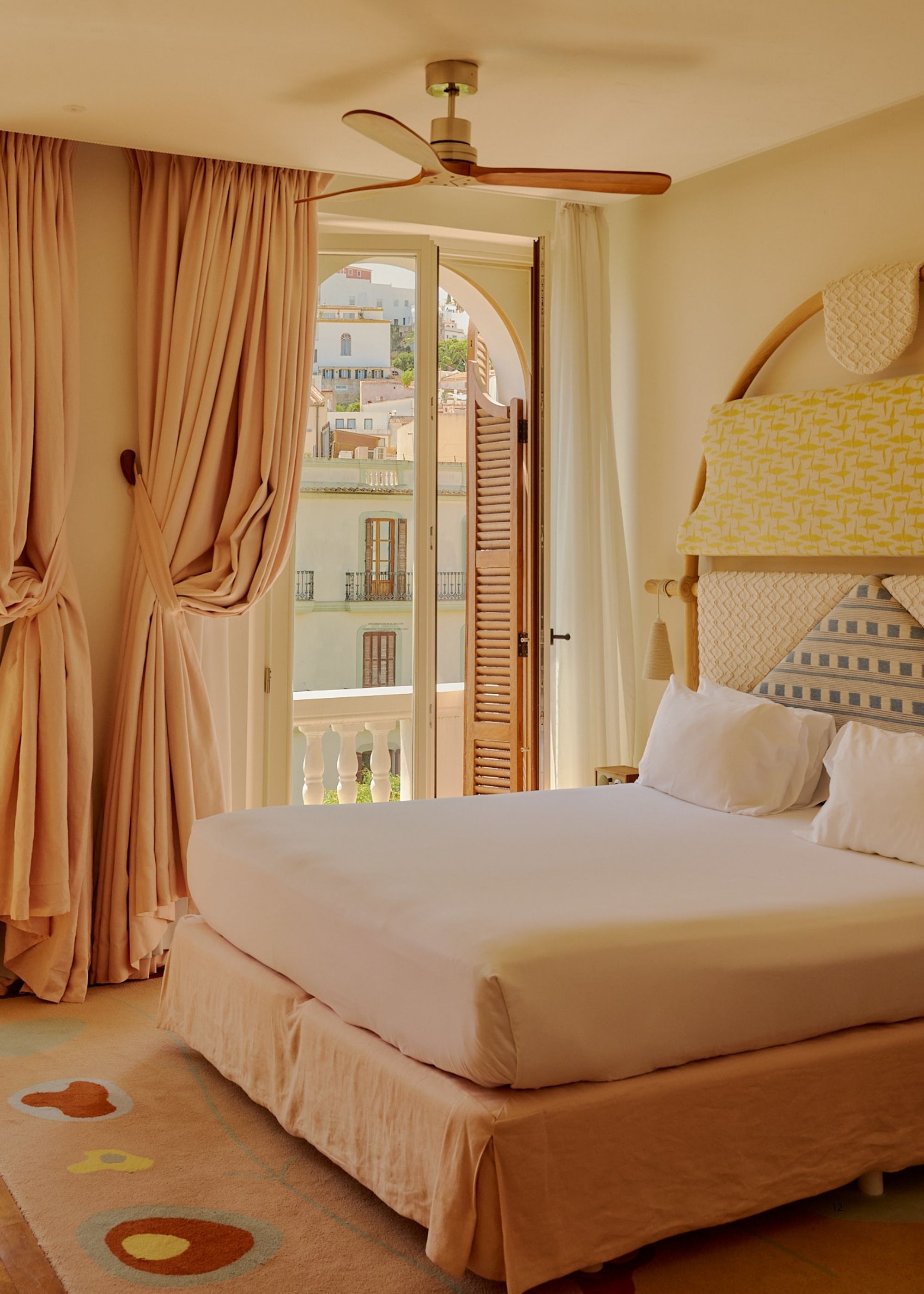 A bright bedroom with off-white walls, peach curtains, and a peach bed that has a sculptural, light yellow headboard.