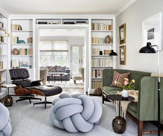 living room with white walls green couch black midcentury chair and stool and built in book shelves