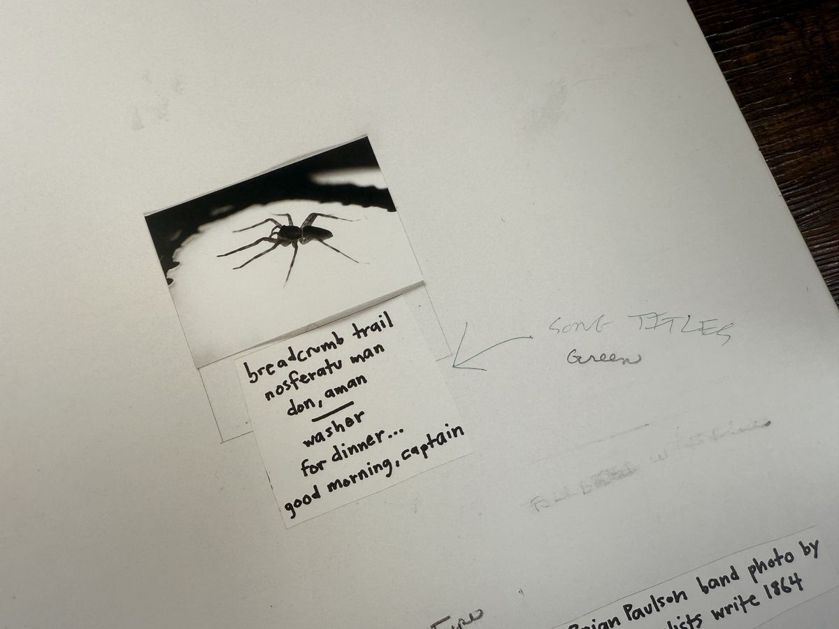 A close-up of the white back cover of Spiderland by Slint. The tracks are listed below a picture of a black spider. Some handwritten text is visible to the left.