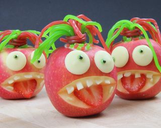 Halloween activities for kids using Pink lady apples carved into edible sweet treats with candy lace sweets, almonds, strawberries and colored icing