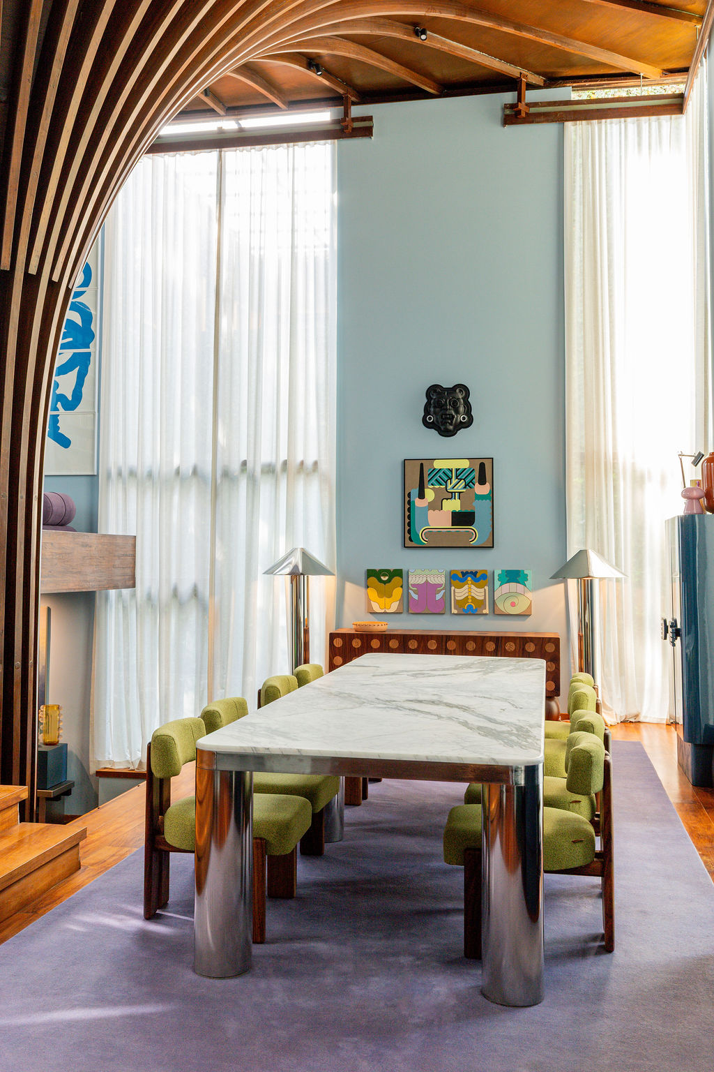 a dining room with lilac rug, marble table with tubular metal legs, bright green dining chairs, blue walls, and sheer curtains