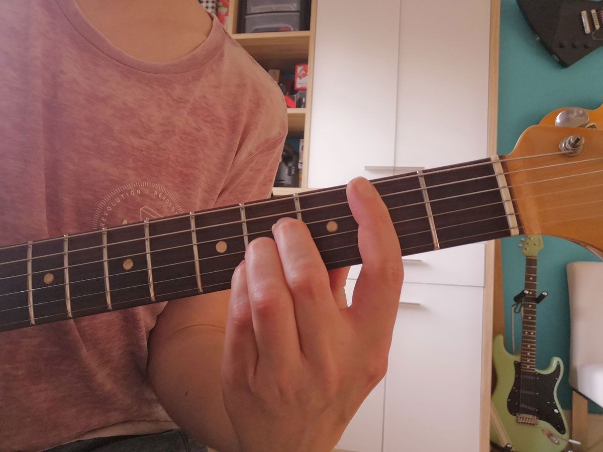 A person playing the A-shape B major barre on electric guitar