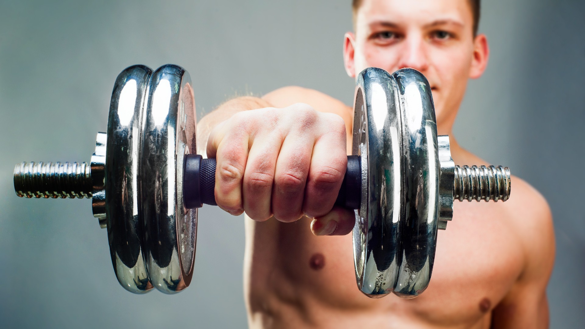 Man holding a dumbbell extended at shoulder height using an overhand grip close-up