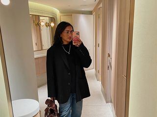 Chiara wears black blazer, blue jeans, and Tabis while posing for a mirror selfie.