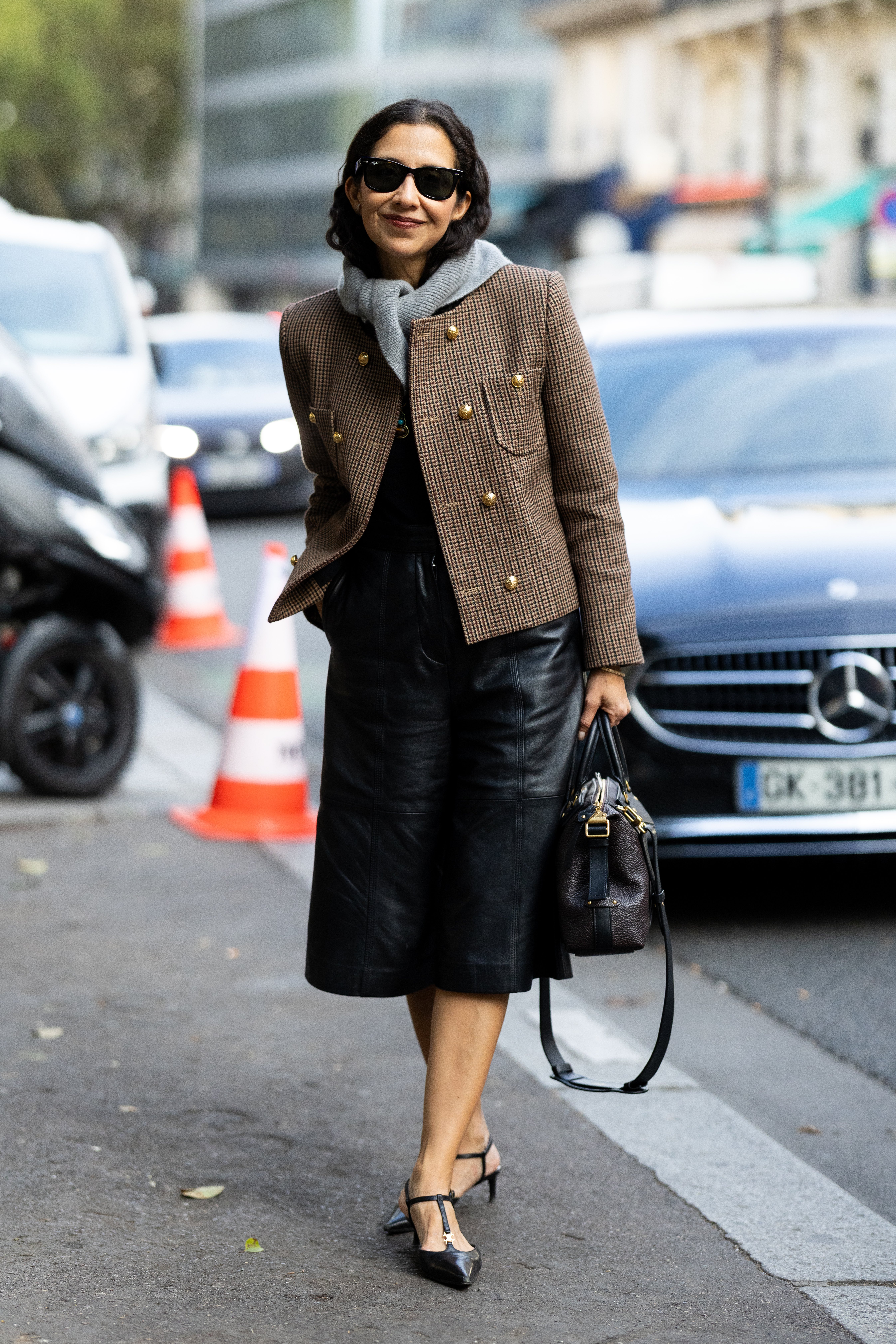 PARIS, FRANCE - OCTOBER 01: Karla Martinez wears a black sweater, black leather heeled slingback, black sunglasses, a grey scarf, a beige checked jacket, a brown and black leather bag and black leather bermuda shorts outside Acne Studios show during the Womenswear Spring Summer 2026 as part of Paris Fashion Week on October 01, 2025 in Paris, France. (Photo by Valentina Frugiuele/Getty Images)