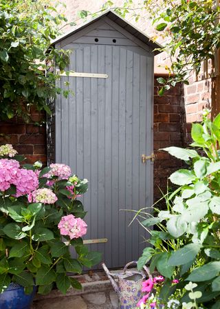 garden mini shed with brick wall pink flower and watering can