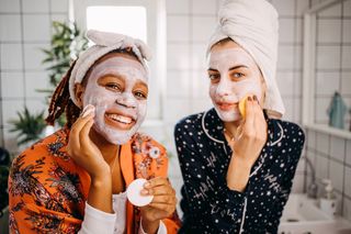 Two friends enjoying a pamper night together in their bathroom while putting face masks on.