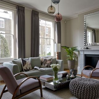 grey living room with large windows, mirror above the fireplace and grey sofa