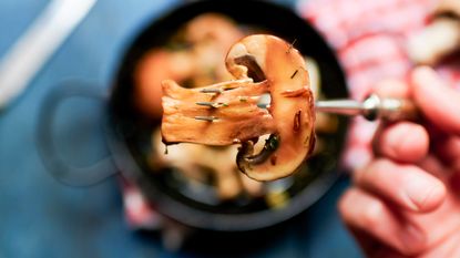 A cooked mushroom is held on a fork above a meal