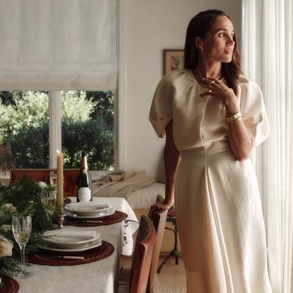 Meghan Markle posing next to a table in a white dress