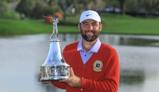 Scottie Scheffler wears a red cardigan and holds the Arnold Palmer Invitational trophy