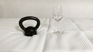 A black kettlebell and a clear wine glass placed on top of the DreamCloud Luxury Hybrid mattress during testing of motion isolation