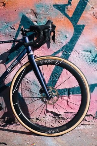 A side on shot of the front end of a blue road bike against a backdrop of some graffiti.