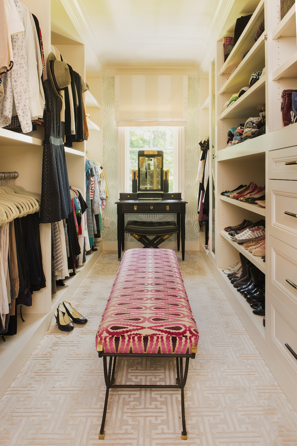 walk in closet with black dressing table and pink patterned ottoman
