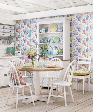 A white dining room with floral wallpaper, a french dresser and a wooden table