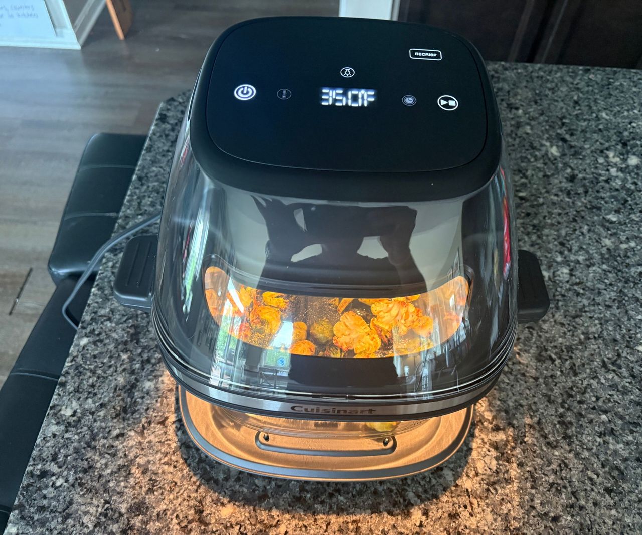 The Cuisinart glass air fryer on a granite countertop turned on with roasted vegetables visible inside.