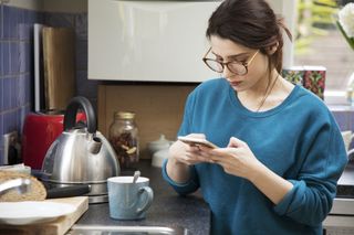 Women in glasses looking at phone while standing next to the kettle in the kitchen
