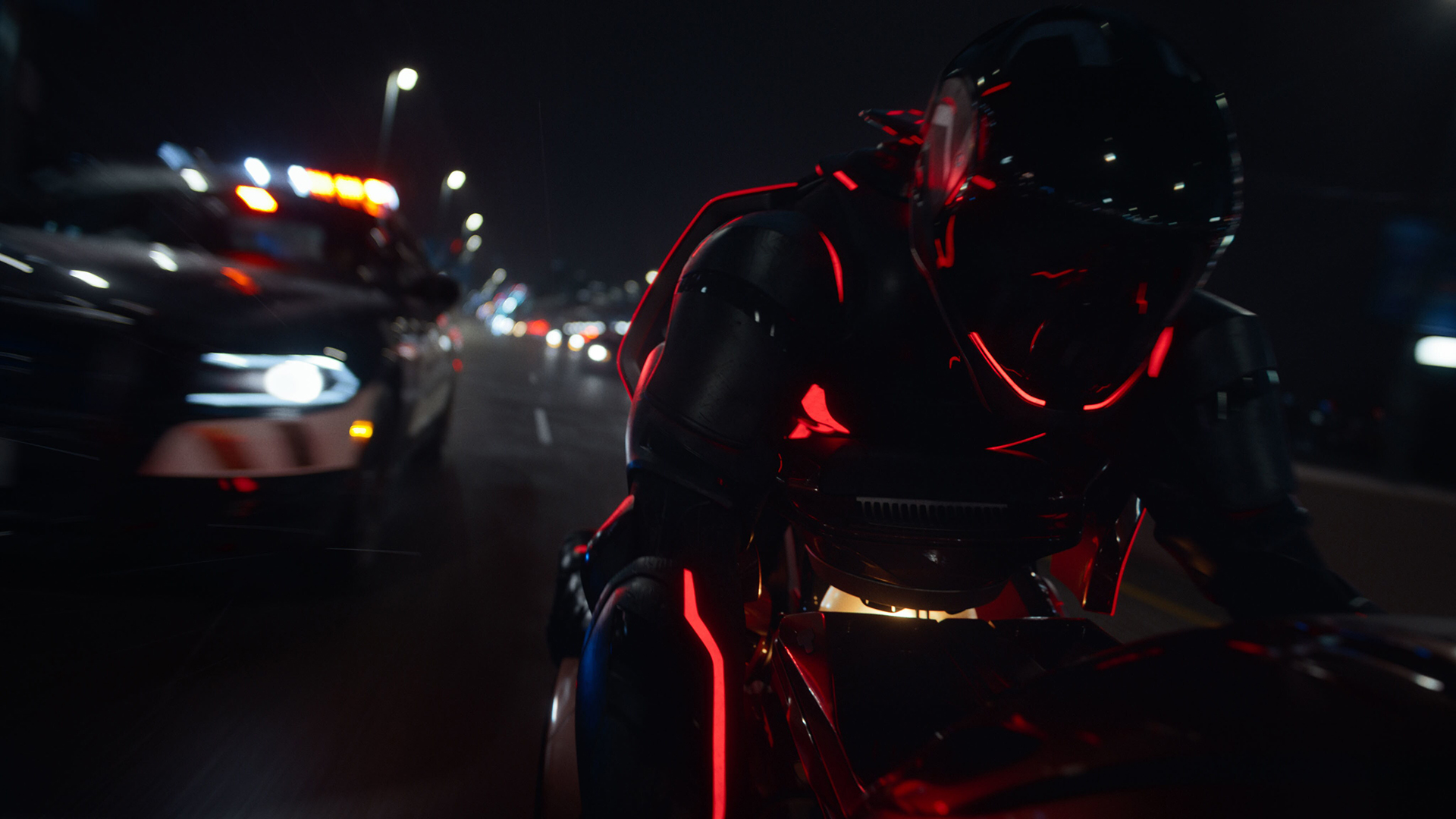 Still from the movie Tron: Ares. It is dark outside and a person is speeding down the road on a Light Cycle (futuristic motorcycle). They are wearing a black bodysuit and helmet, both with red light trim. They are being chased by a police car.