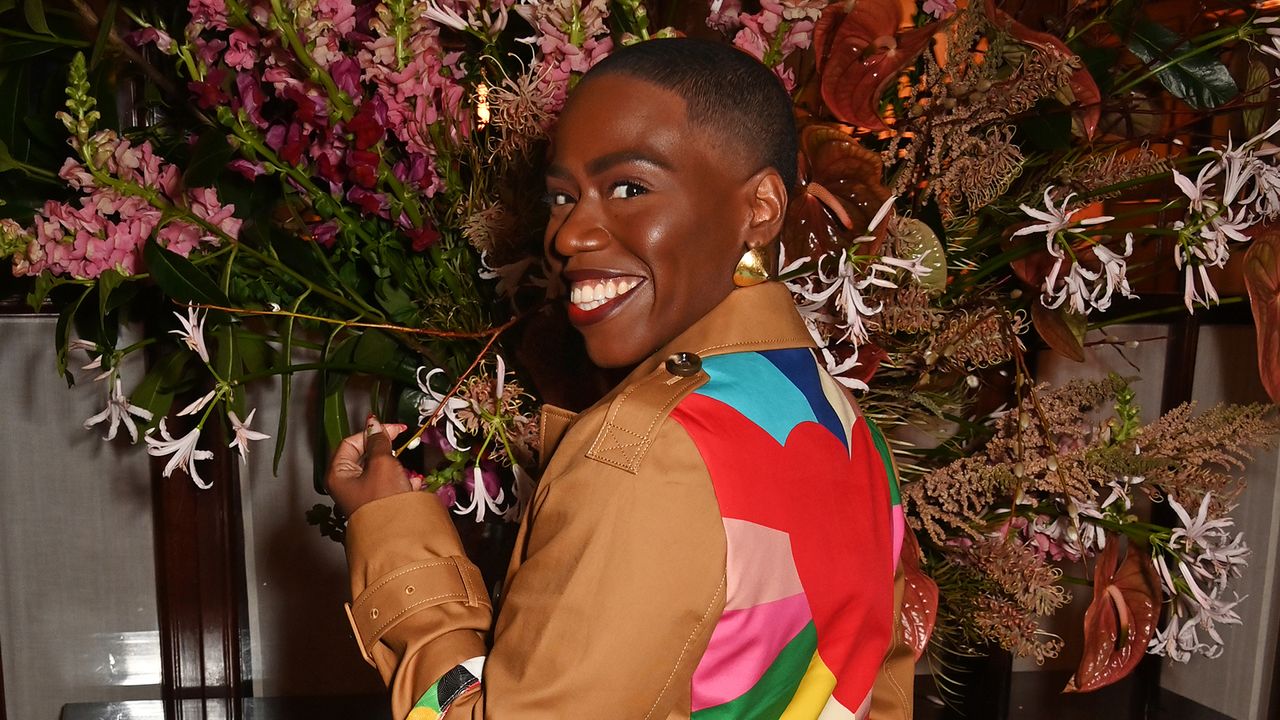 Candice Brathwaite wearing a leather coat with a colourful back standing in front of a flower display