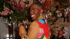 Candice Brathwaite wearing a leather coat with a colourful back standing in front of a flower display