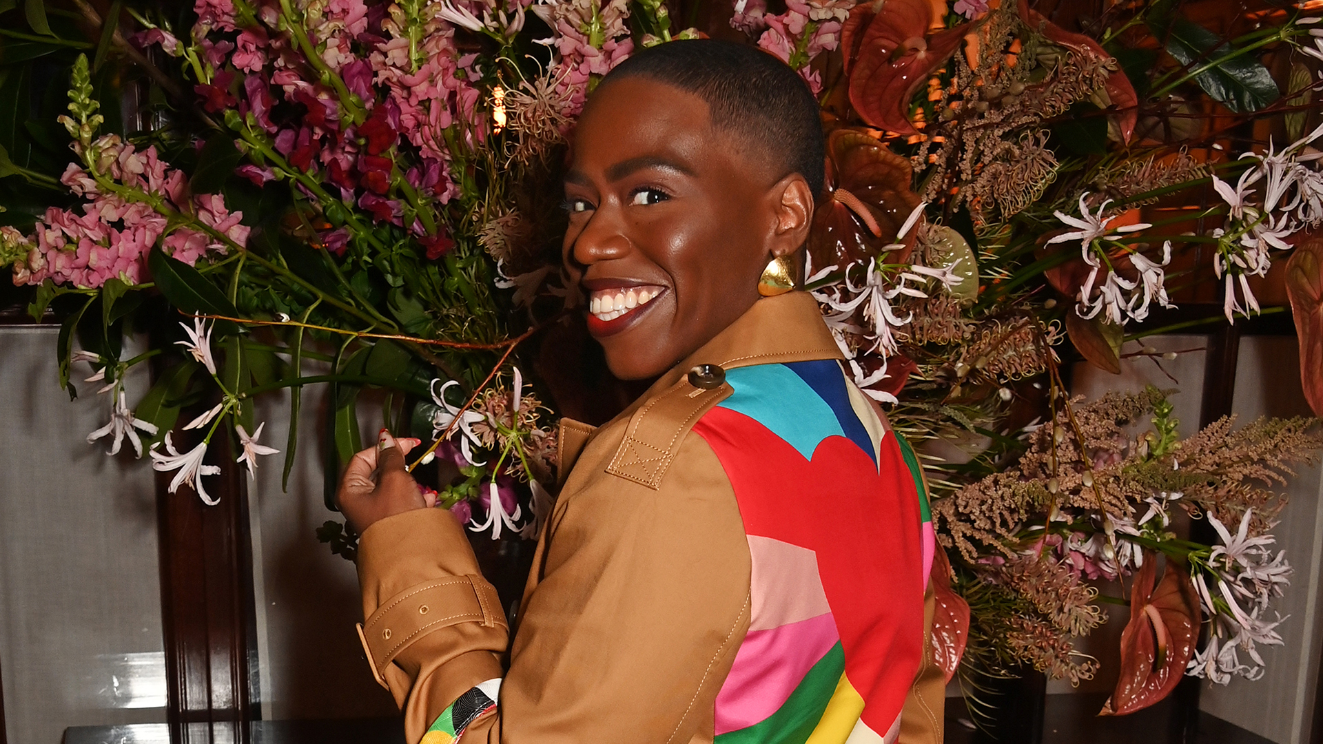 Candice Brathwaite wearing a leather coat with a colourful back standing in front of a flower display