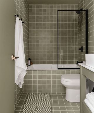 A green tile drenched bathroom using square tiles and white grout and black hardware