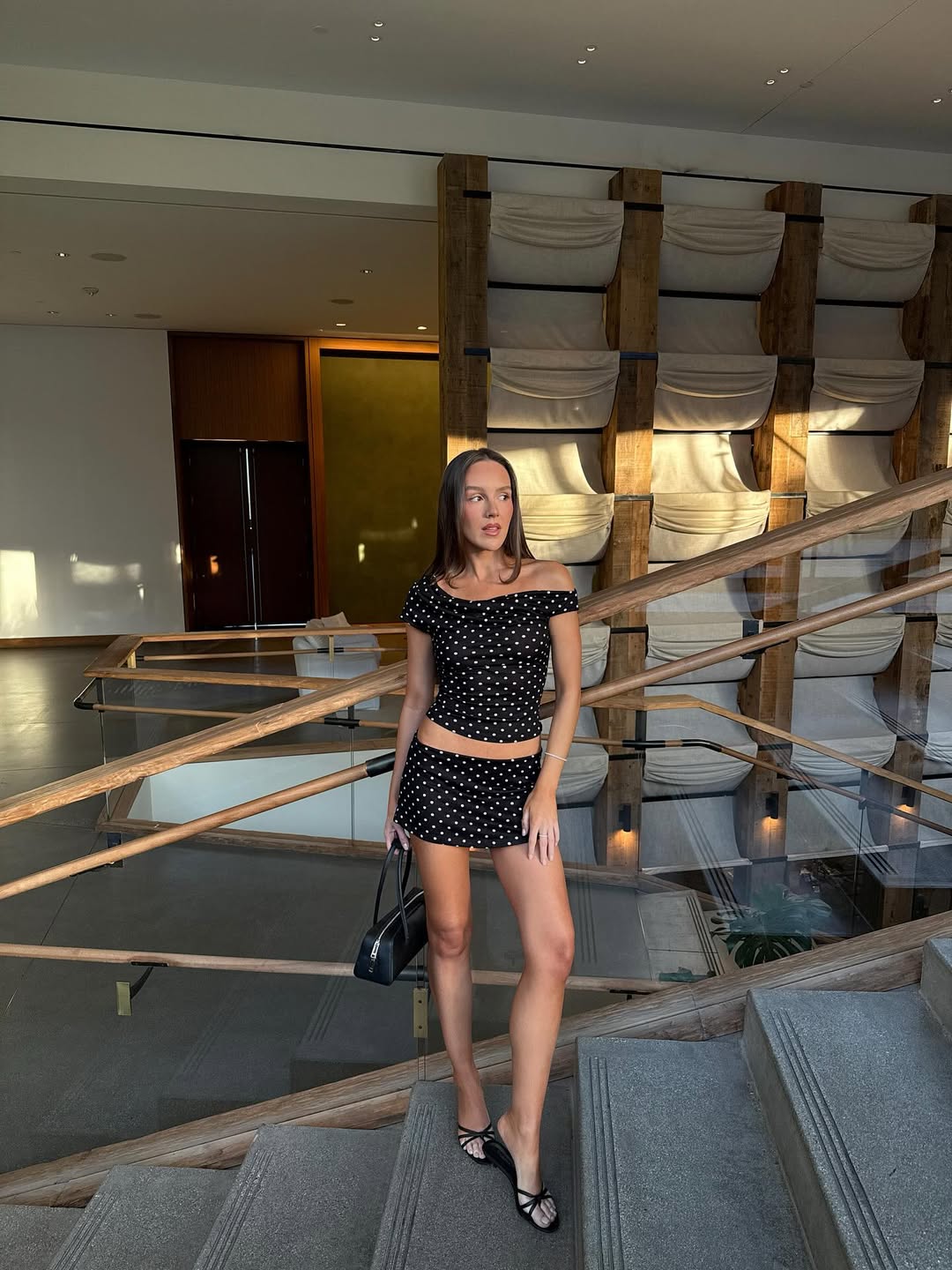 Influencer Emma Leger in a black strappy sandal, polka dot two piece set and E/W bag