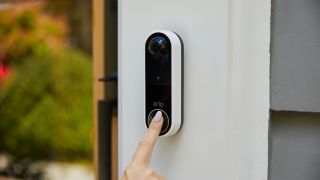 En finger trykker på Arlo Essential Wire-Free Doorbell.