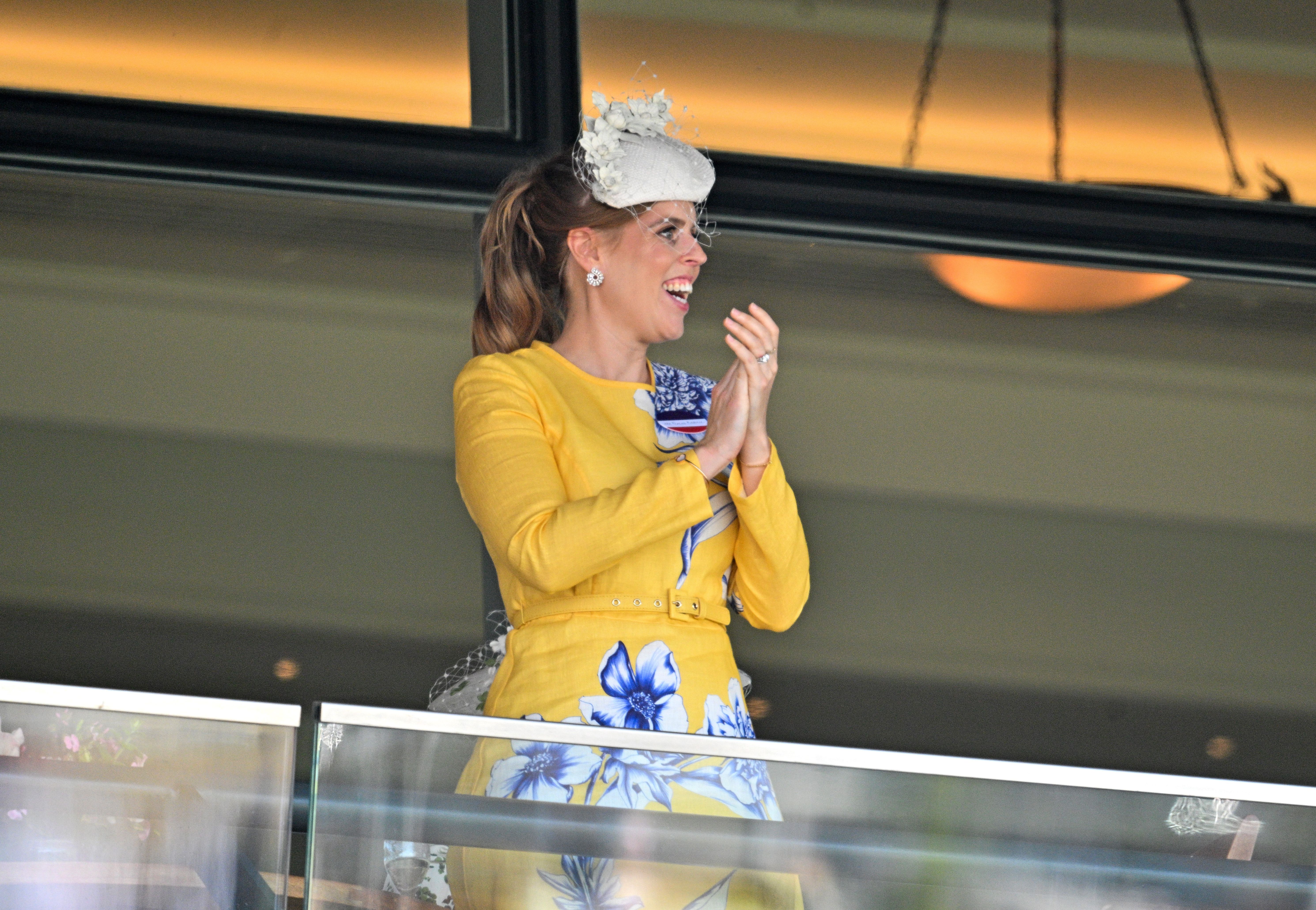 Princess Beatrice wearing a yellow floral dress clapping and smiling at Royal Ascot