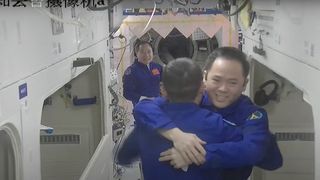 two chinese astronauts hugging aboard the tiangong space station while a third crewmate looks on in the background.