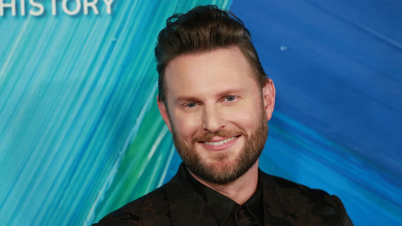 Bobby Berk&#039;s decluttering hack is genius. Here is the interior designer with brown hair, blue eyes, and a beard wearing a black blazer and shirt, in front of a blue painted background