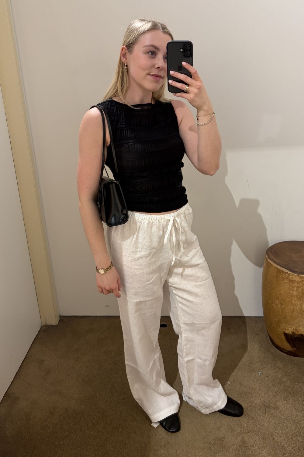 Woman wears black top, white trousers, carries black bag