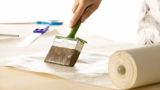 Hand applying wallpaper paste to wallpaper using brush