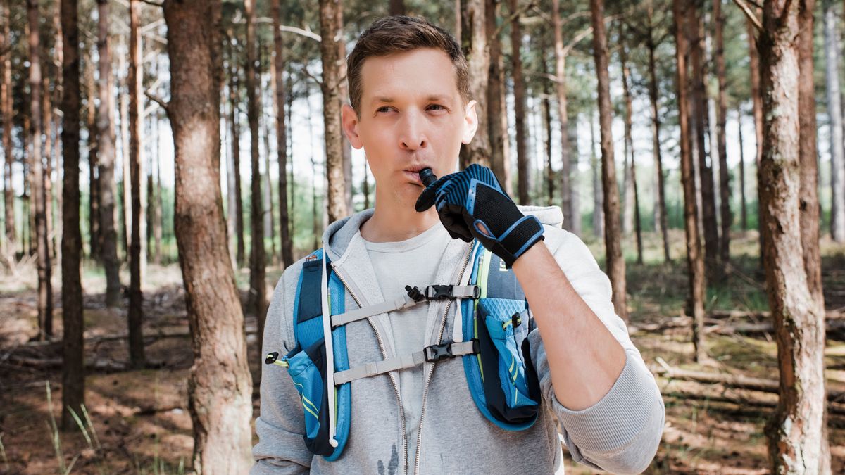 A man drinking from a bladder in his running vest whilst in the forest