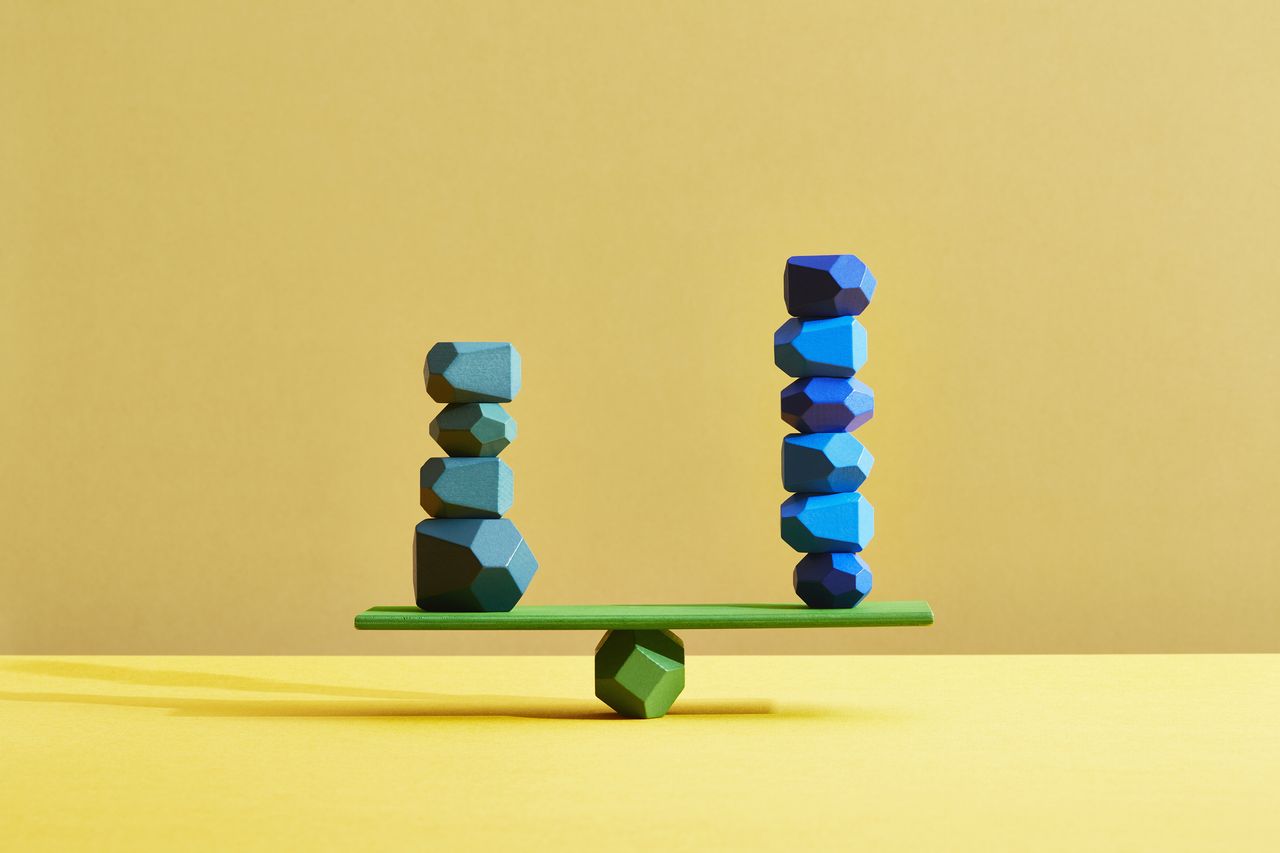 two stacks of teal and blue pebbles balanced on a seesaw