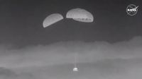 black and white photo of a space capsule descending through the sky under three parachutes