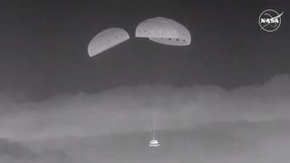 black and white photo of a space capsule descending through the sky under three parachutes