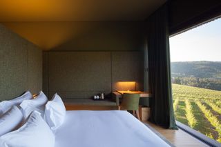 A room in the Hotel Monverde. A large bed covered in white linen sits across the floor-to-ceiling window that looks out to the vineyards.