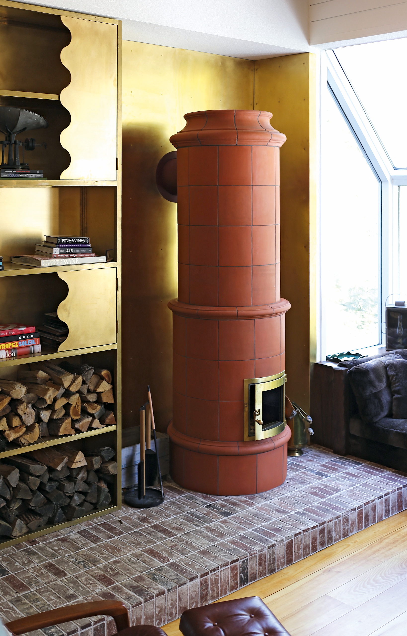 Terracotta kachelofen on a brick platform with a brass backdrop