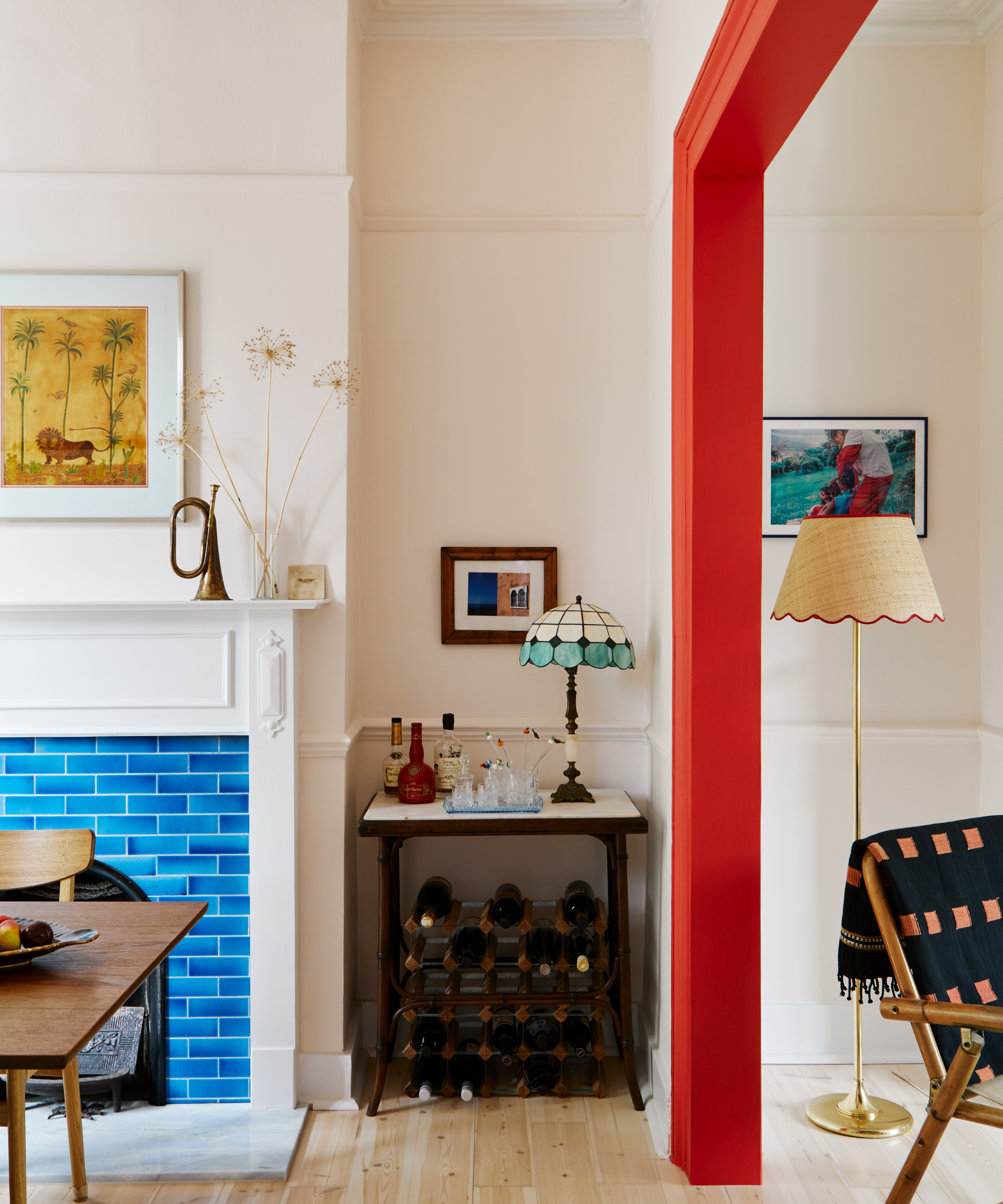 a bright red doorframe that separates two rooms. On the left is a dining room with a bright blue tiled fireplace and a wine rack underneath a small bar table.