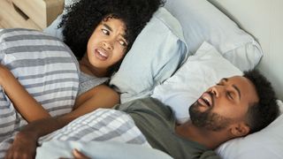 Woman looking angrily at her partner, who is snoring