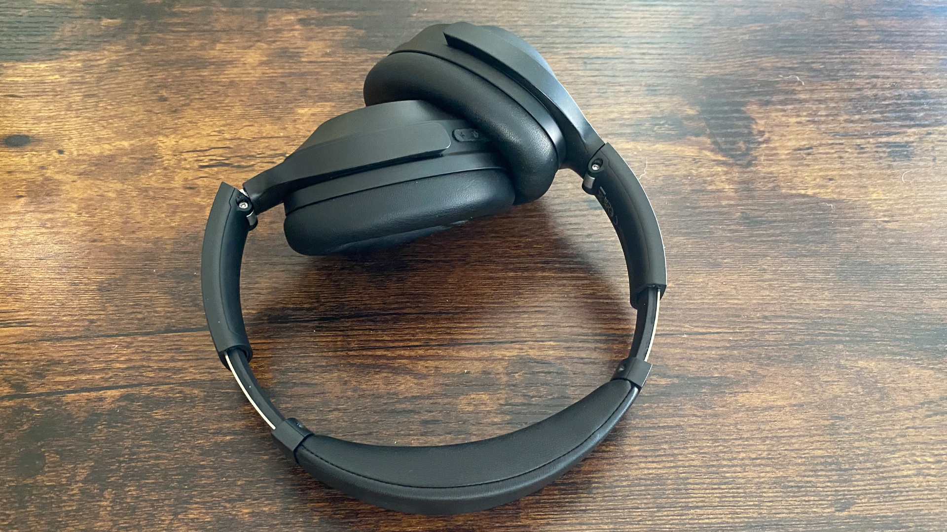 Earfun Wave Life over-ear headphones, the earcups folded inwards, on a wooden surface