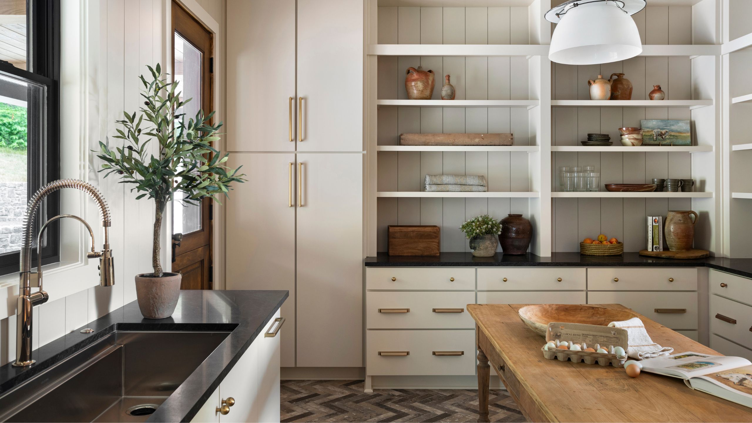 a neutal vintage inspired scullery kitchen with open storage units and a farmhouse table in the center
