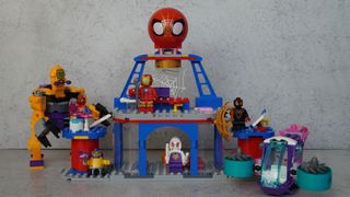 A complete Lego set featuring a purple helicopter, a yellow alien/robot, minifigures and a giant Spider-Man head is placed on a grey background.