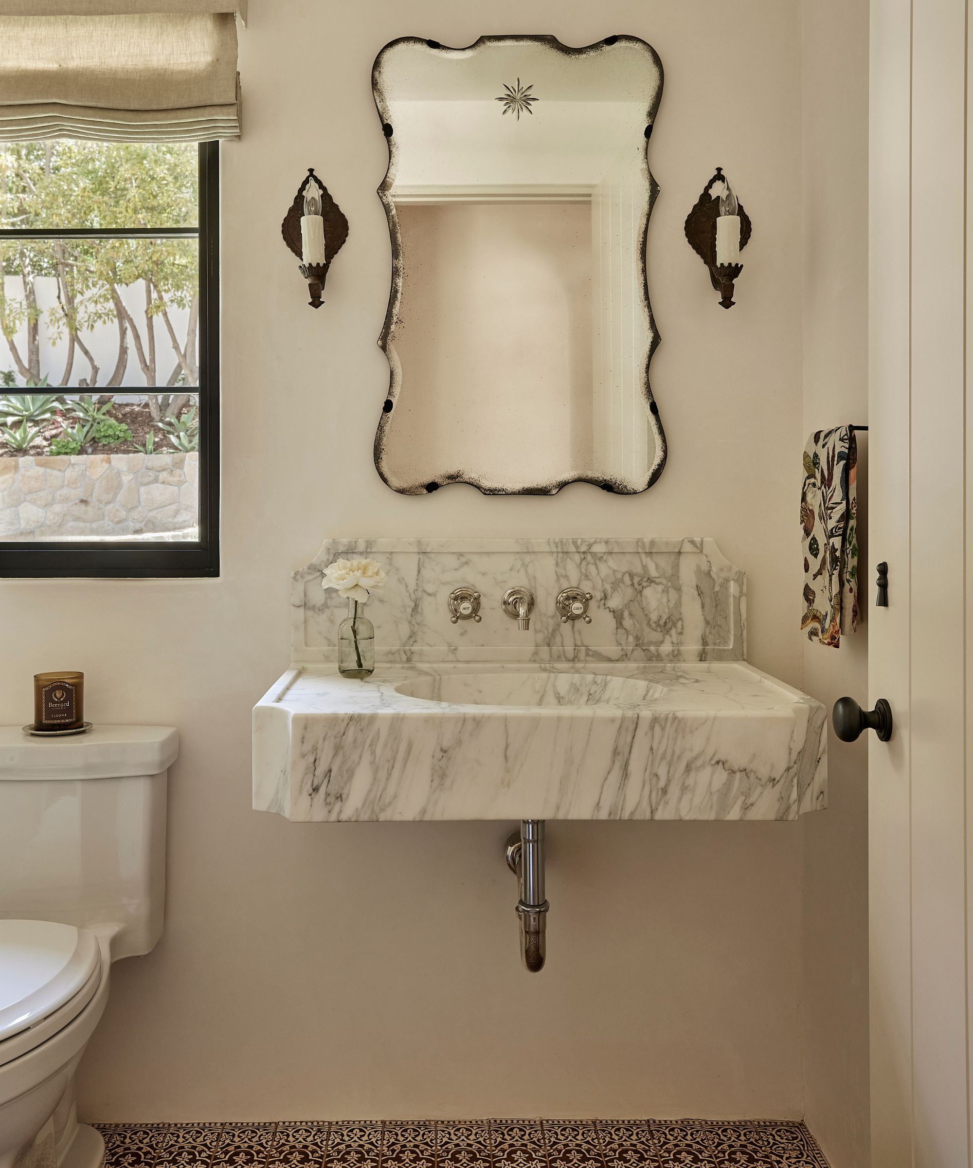 a neutral powder room with large marble sink, terracotta floors and vintage mirror and sconces