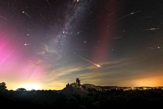 a view of the night sky with an old castle ruin in the foreground. There is a pink hue on the left which is the northern lights and lots of streaks of light which are the perseid meteor and toward the center right of the image is a long red glow which is known as a SAR arc.